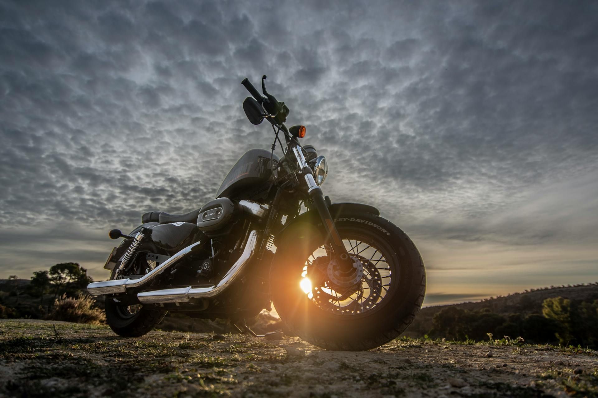 A motorcycle is parked on top of a dirt hill at sunset.