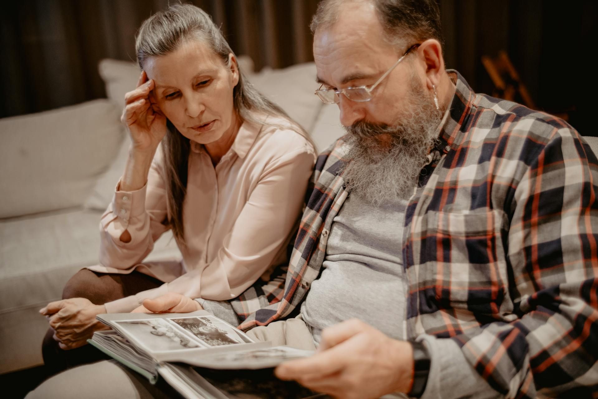 A man and a woman are sitting on a couch looking at a photo album.