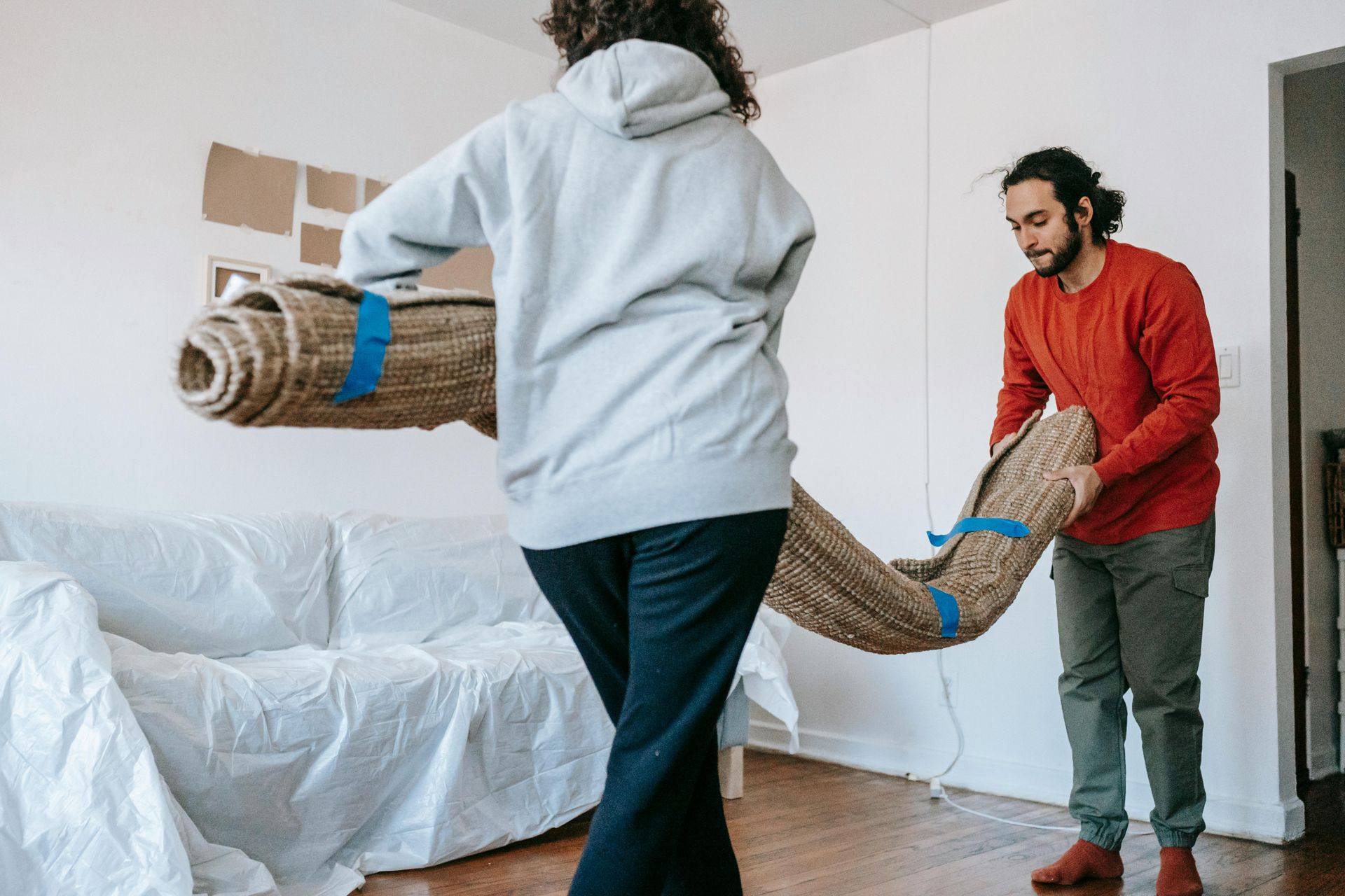 A man and a woman are rolling a rug in a living room.