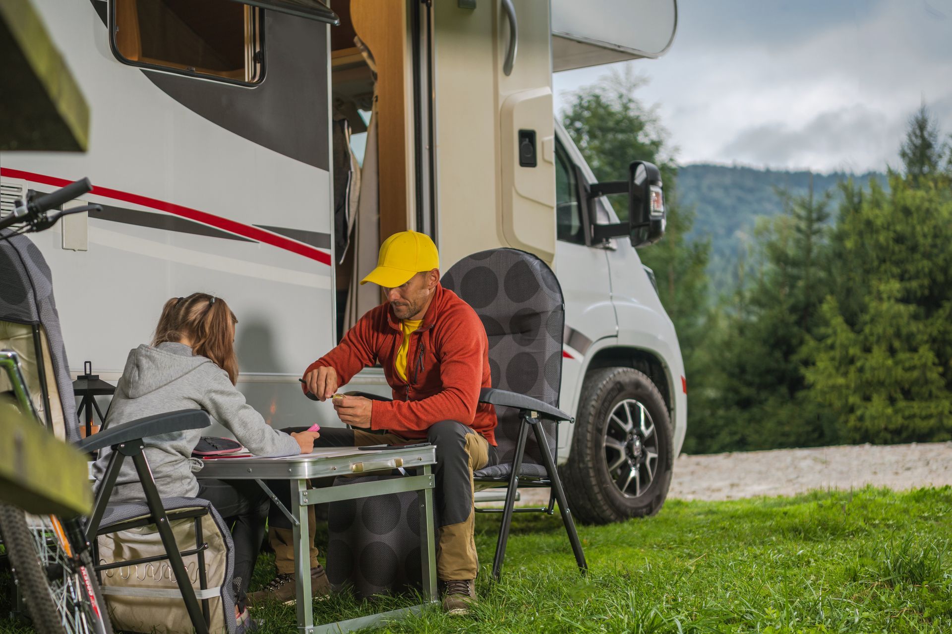 A man and a woman are sitting outside of a rv.