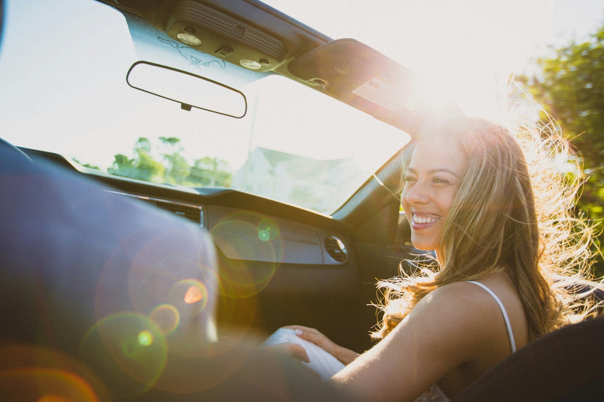 A woman is sitting in the driver 's seat of a convertible car.