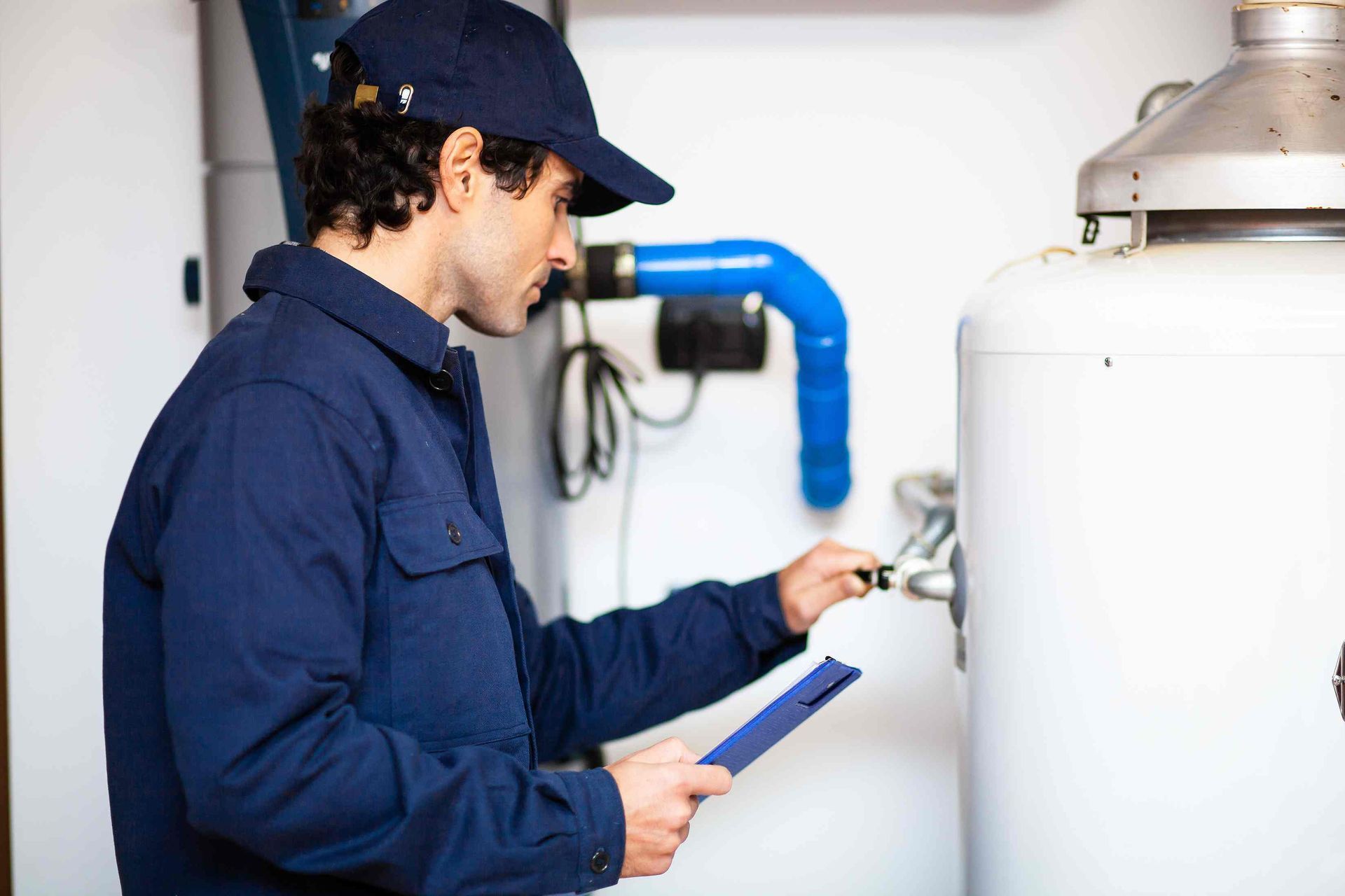 An HVAC technician holding a clipboard and performing an inspection on a residential water heater at