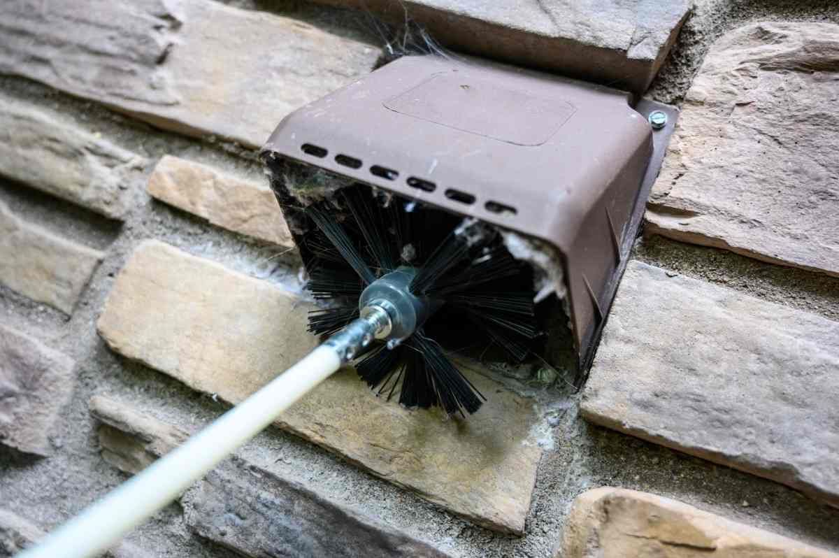 Clogged dryer vent on a home's exterior with stone siding getting cleaned by a spinning brush at Advantage Air HVAC near Lexington, KY