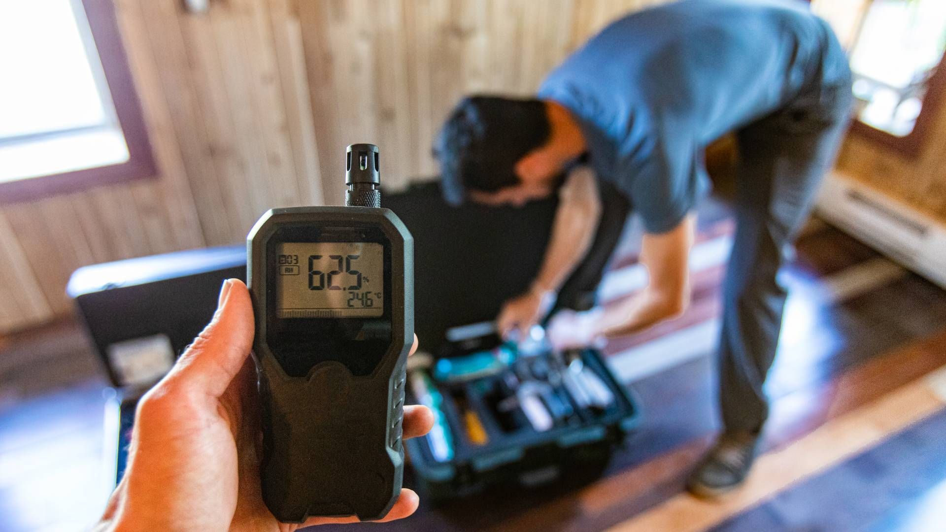 Person holding an indoor air quality meter in front of another person with a case full of testing eq