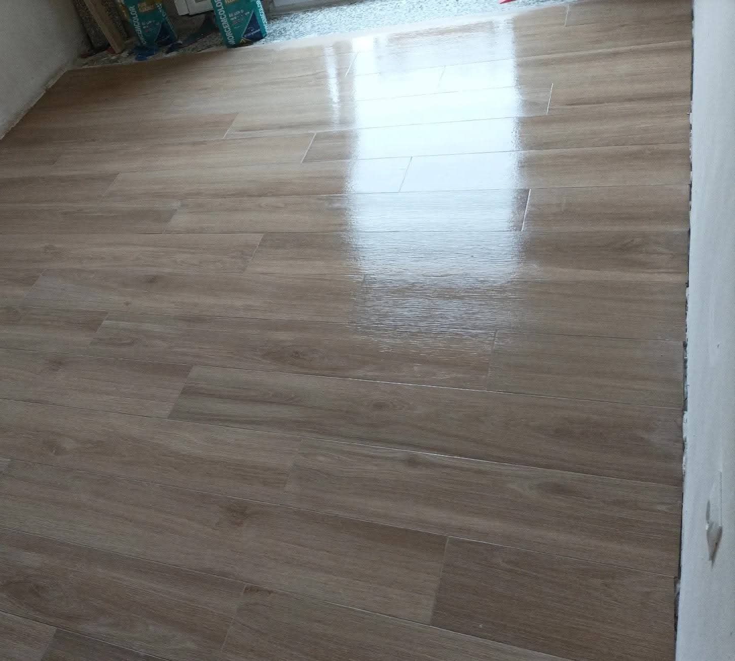 Un piso de madera en una sala de estar con el reflejo de una ventana.