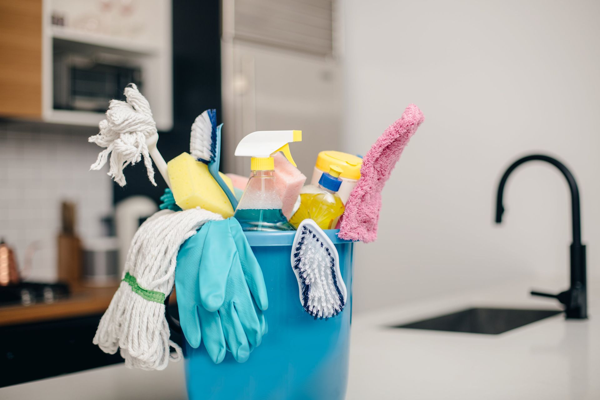 Blue cleaning caddy with spray bottles, sponges, cloths, and gloves on a kitchen counter