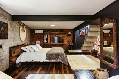 Cozy bedroom with wooden bed, stone walls, staircase, and large mirror in a warm rustic interior