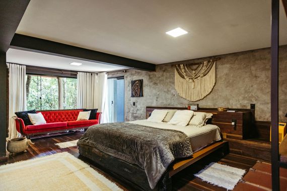 Spacious bedroom with a large bed, red sofa, and bay window in a modern rustic interior