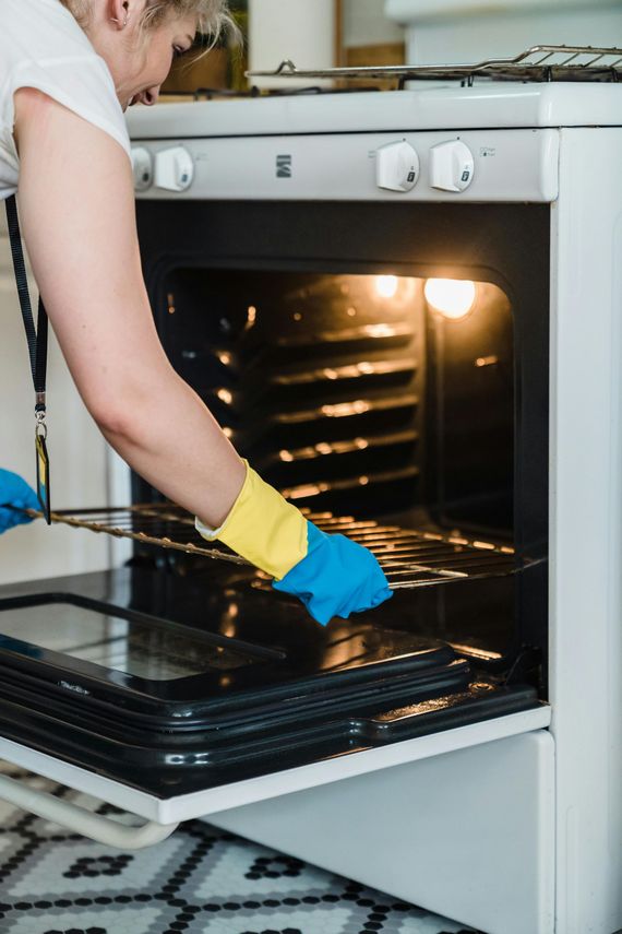 Person cleaning an oven with blue and yellow gloves, oven door open and light on