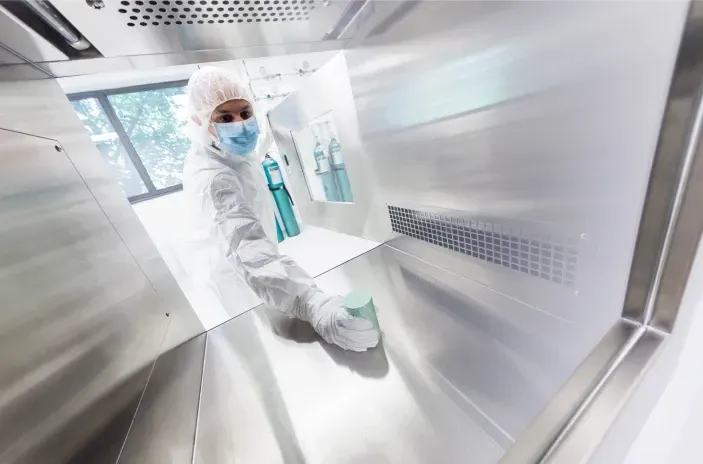 A technician handles a lead-lined safety vessel containing a radiopharmaceutical vial.