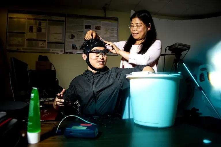 A participant holds his hand in a bucket of ice while Yingzi Lin monitors his pain response.