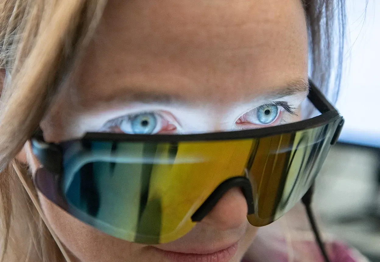 Woman's face with visor-style sunglasses shining light into her blue eyes.