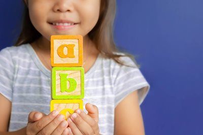 Child holding colorful alphabet blocks with letters a, b, and c against a blue background