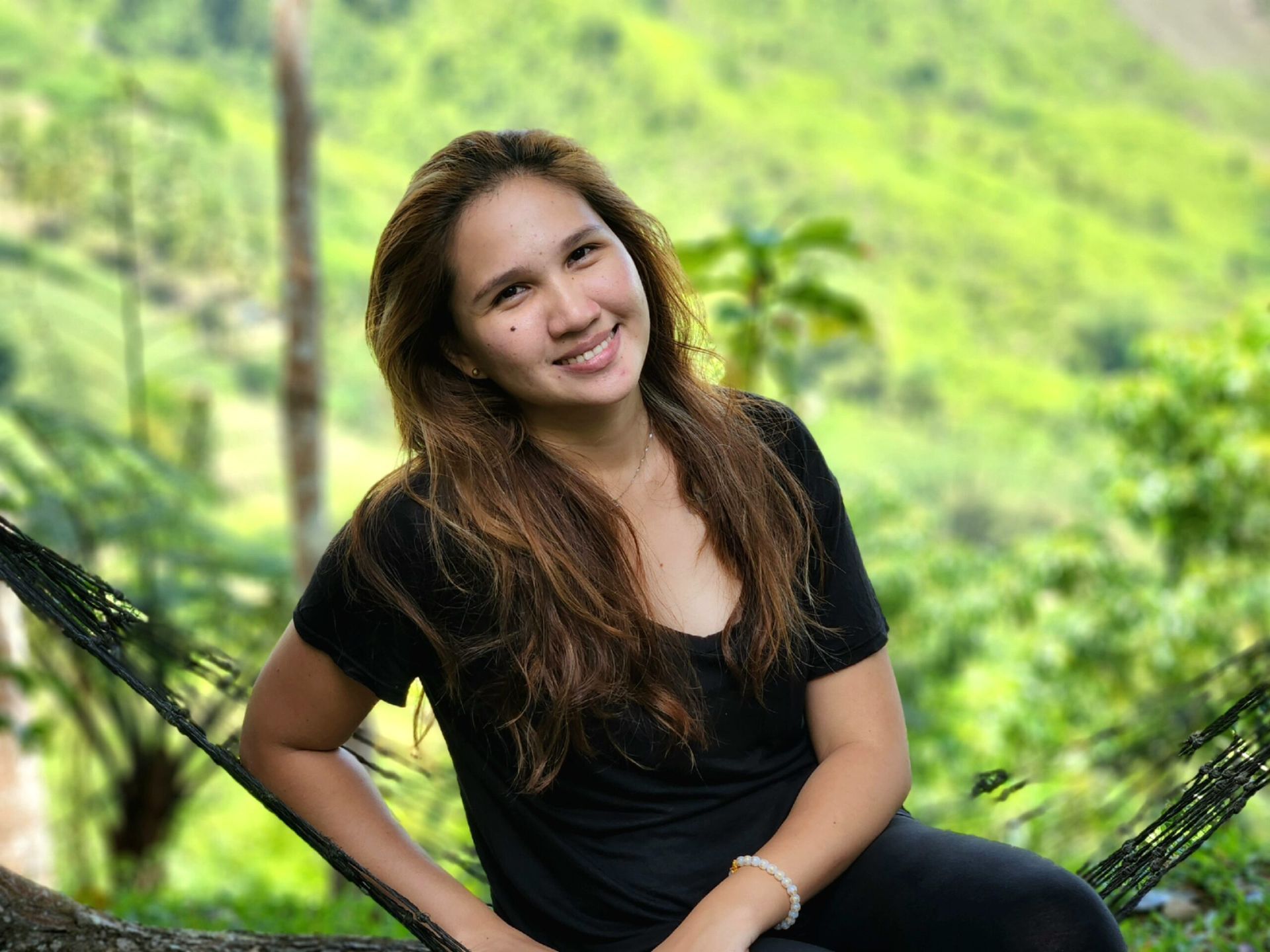 A woman in a black shirt is sitting in a hammock and smiling.