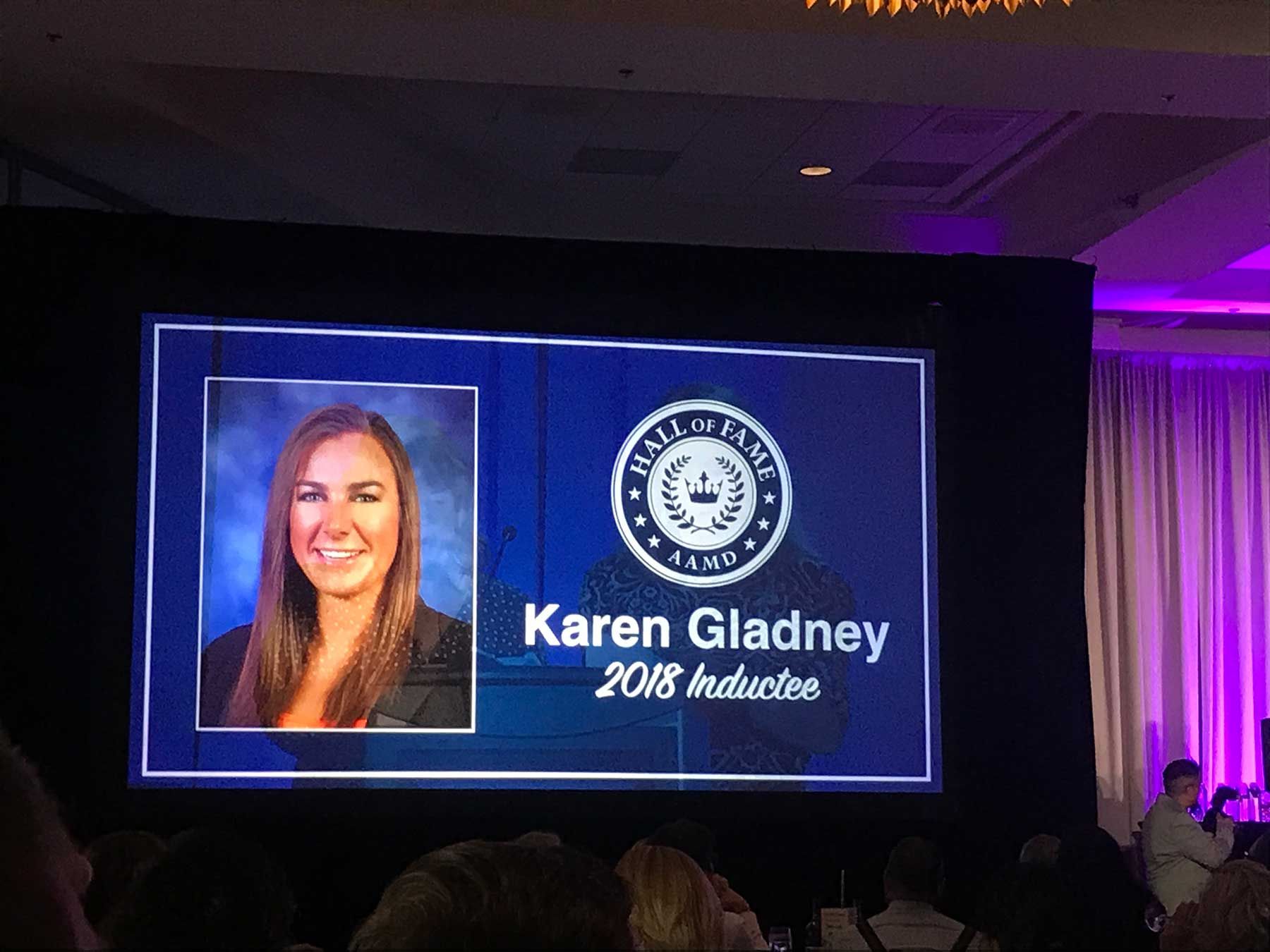 A woman is sitting in front of a large screen that says karen gladney on it.