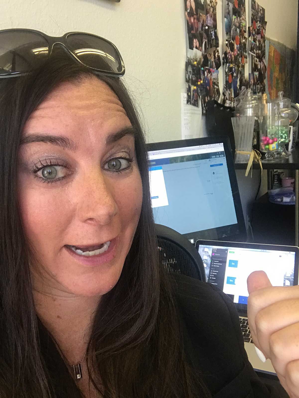 A woman wearing sunglasses is giving a thumbs up in front of a laptop computer.