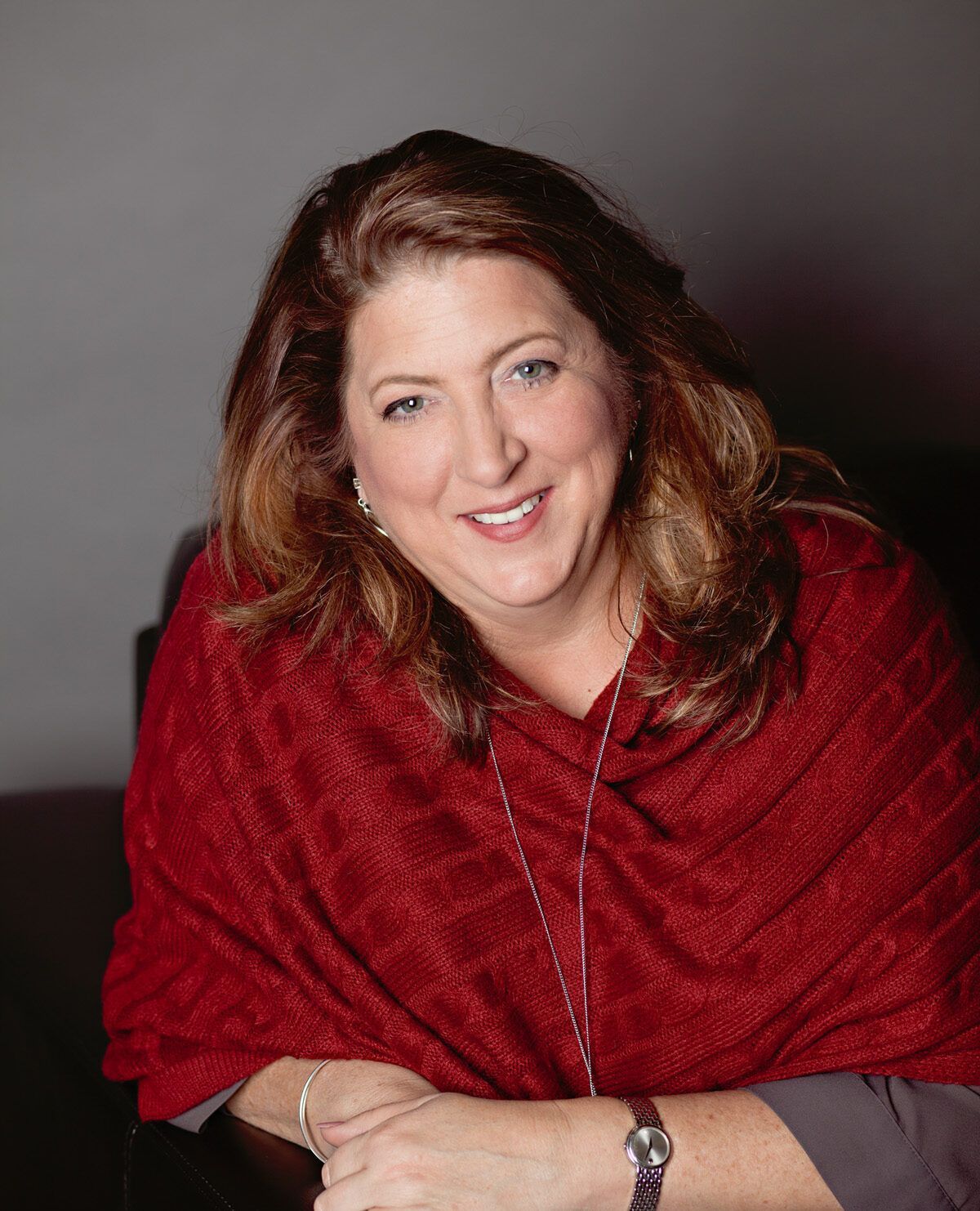 A woman wearing a red scarf and a watch is smiling for the camera.