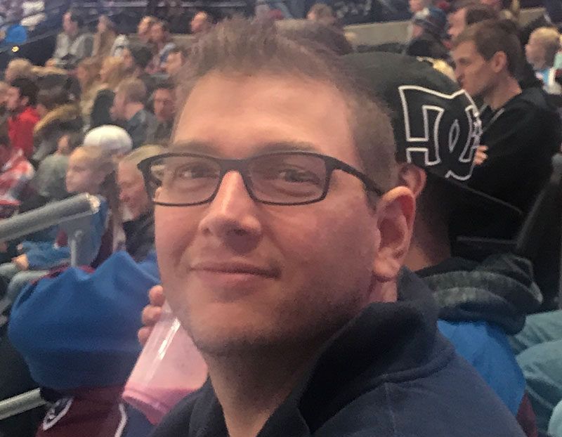 A man wearing glasses and a dc hat is sitting in a stadium.