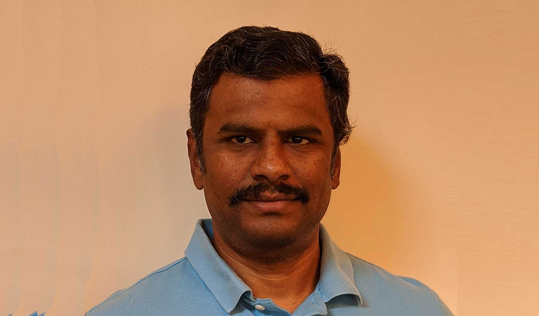 A man with a mustache is wearing a blue shirt and looking at the camera.