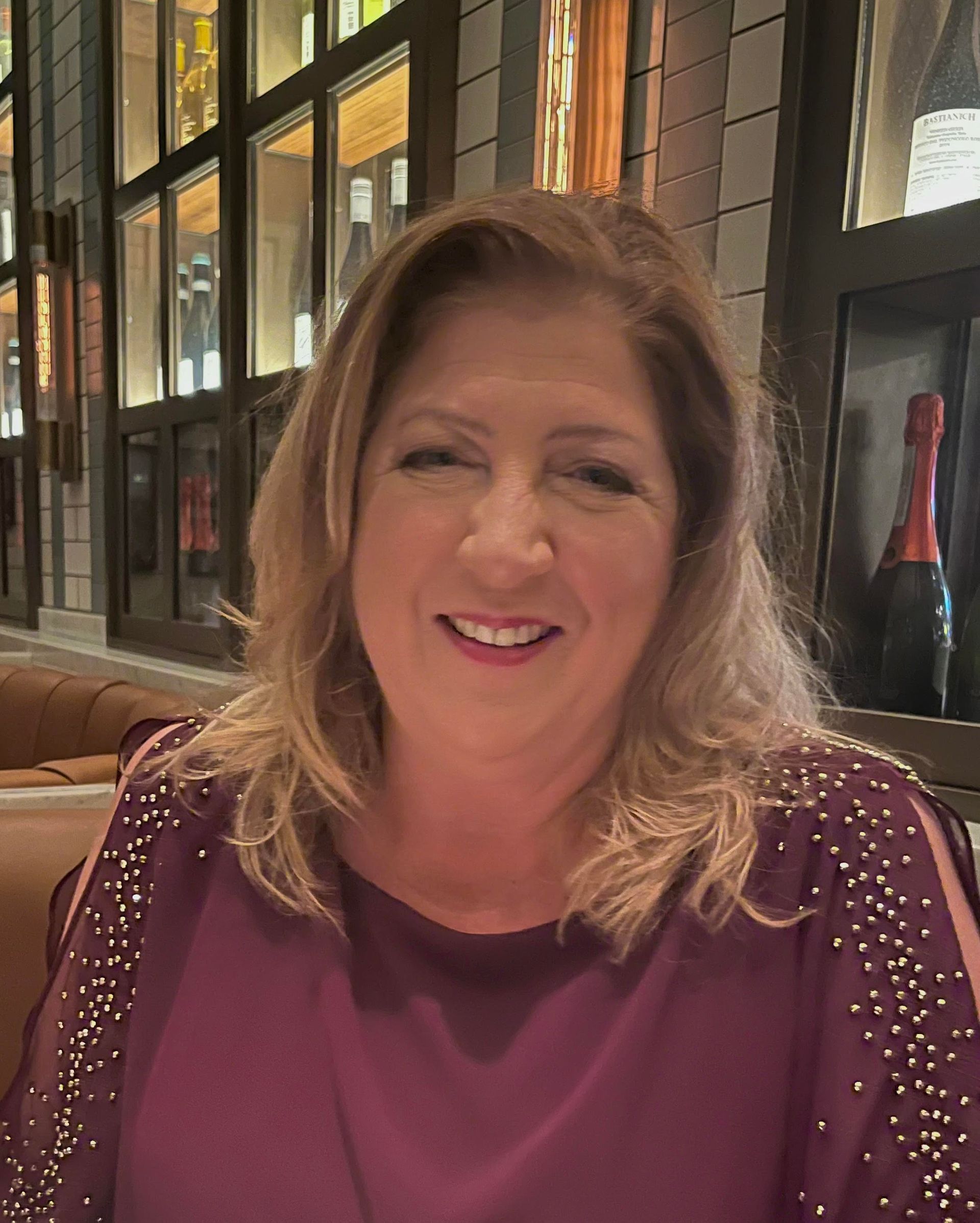 A woman in a purple shirt is smiling while sitting at a table in a restaurant.
