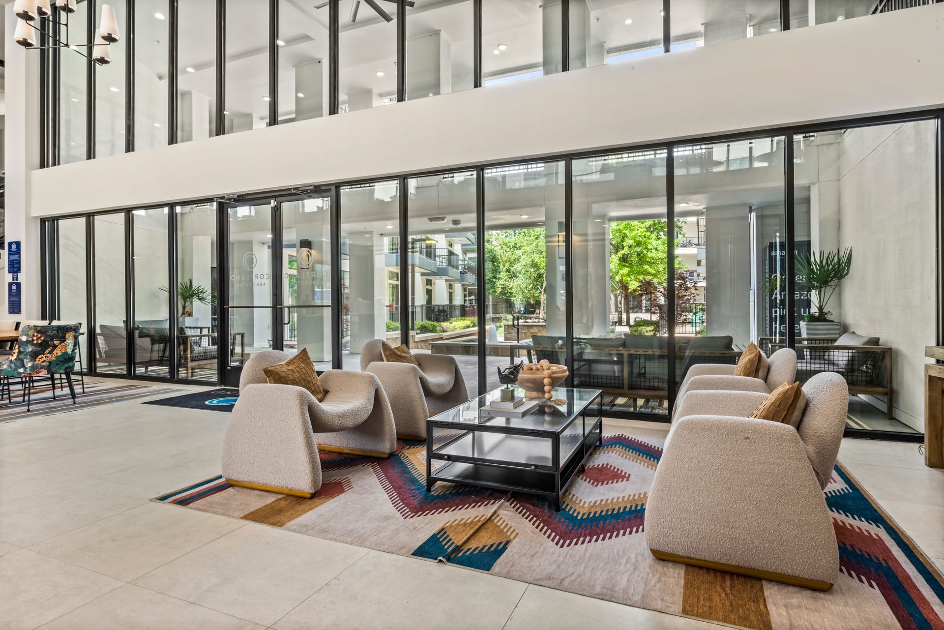 Lobby with seating area, glass walls, and colorful rug. Neutral tones with natural light, inviting space.