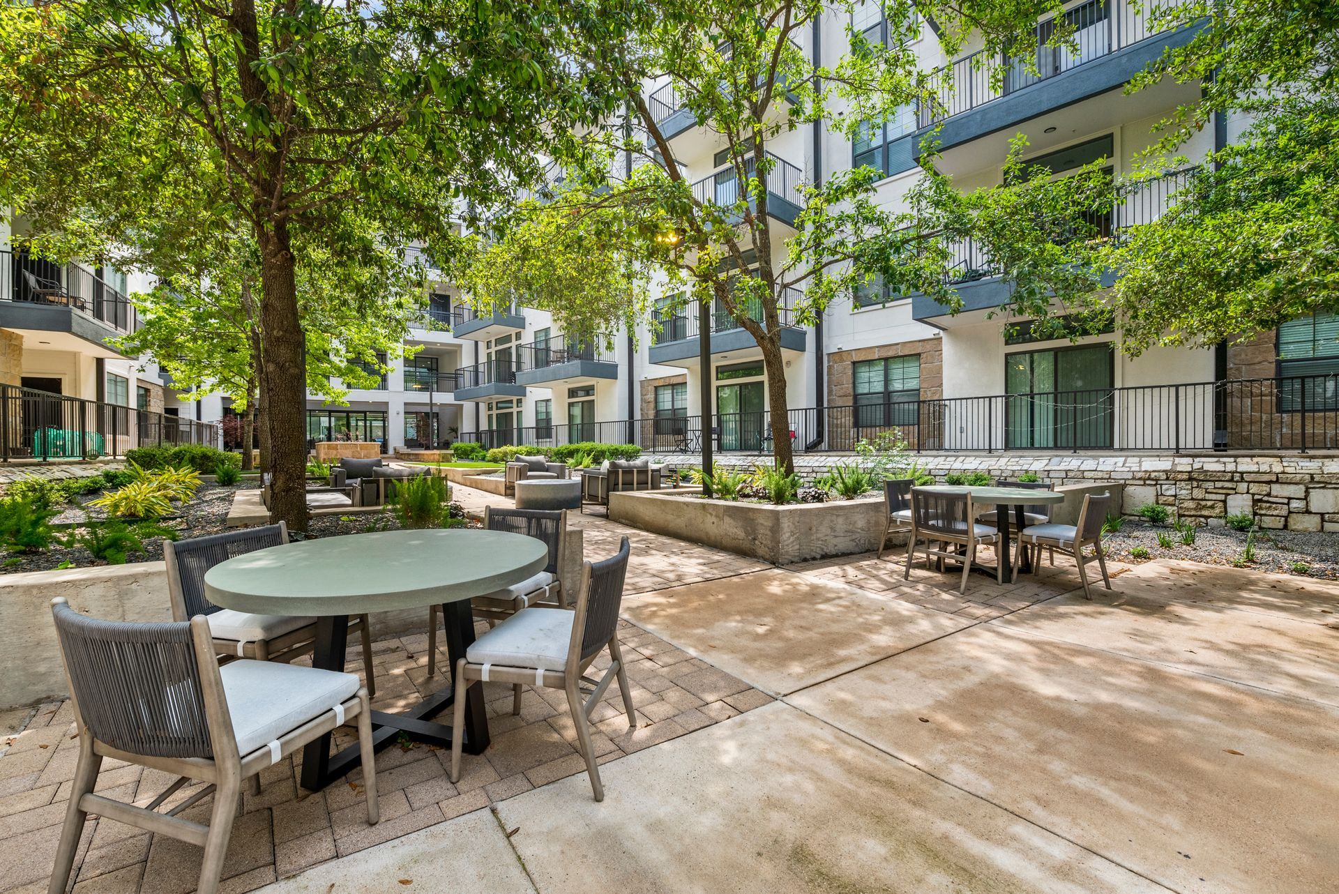 Outdoor patio with tables and chairs, surrounded by trees and modern buildings.