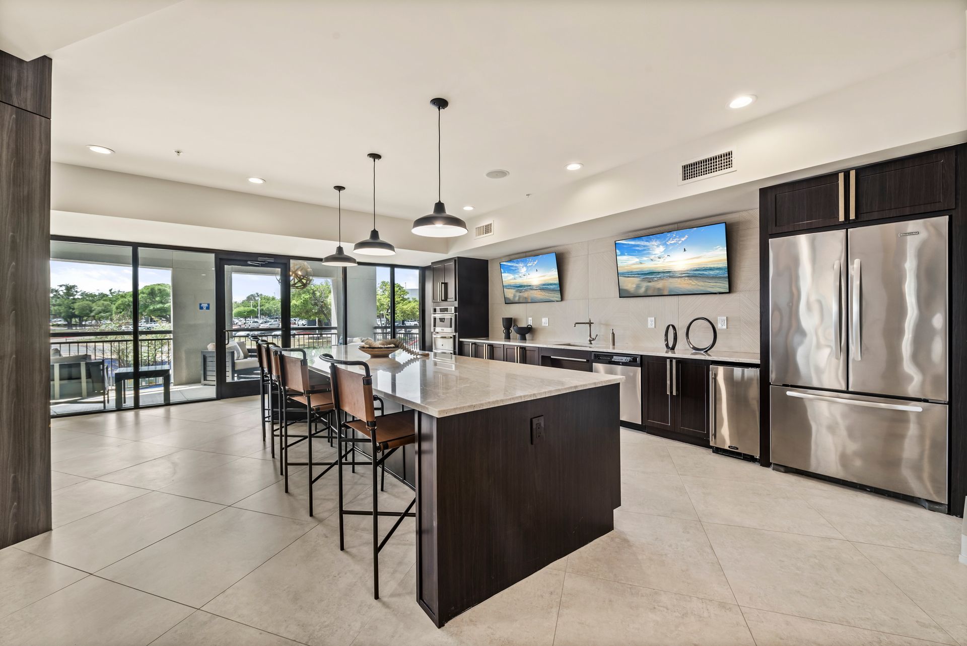 Modern kitchen with island, dark cabinetry, stainless appliances, two TVs, and access to a patio.