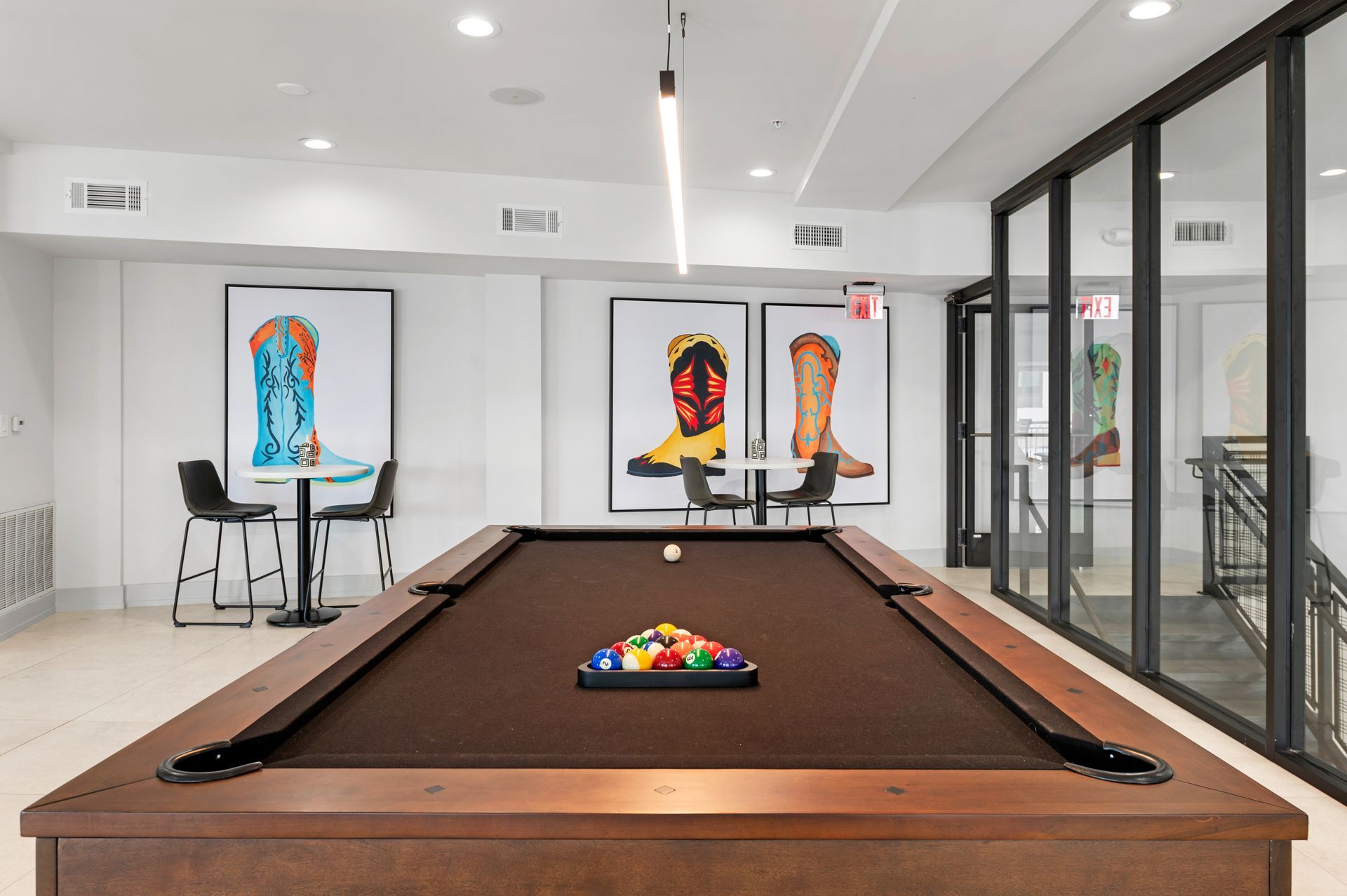 Pool table in a recreational room with colorful art, a staircase, and two small tables with chairs.