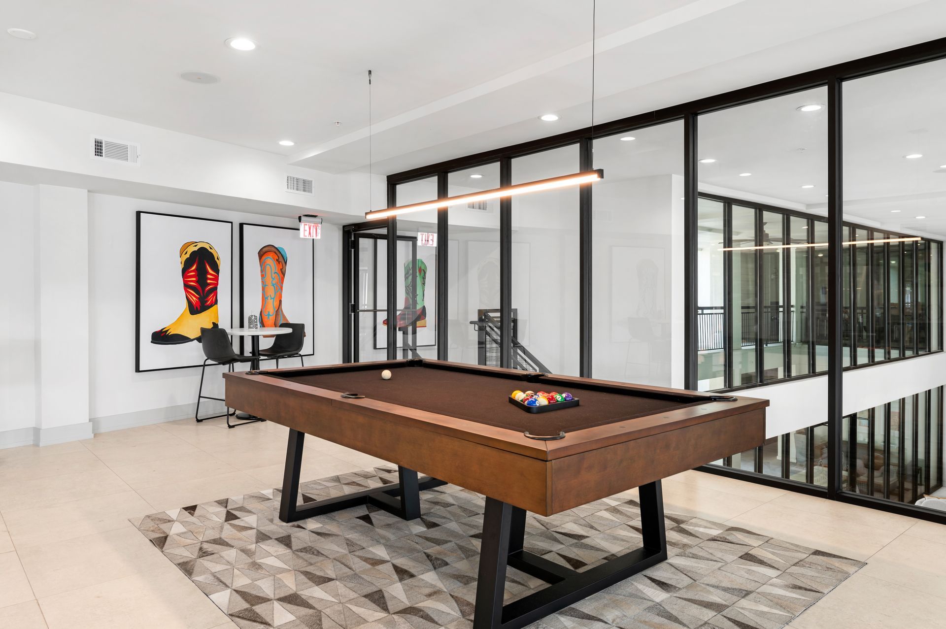 A pool table in a modern game room with artwork and glass walls.