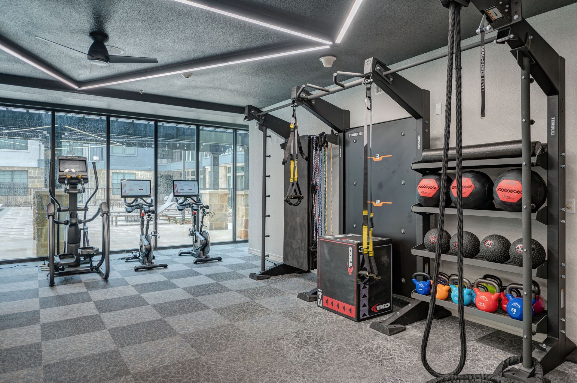 Gym interior with exercise machines, weights, and a mirrored wall.