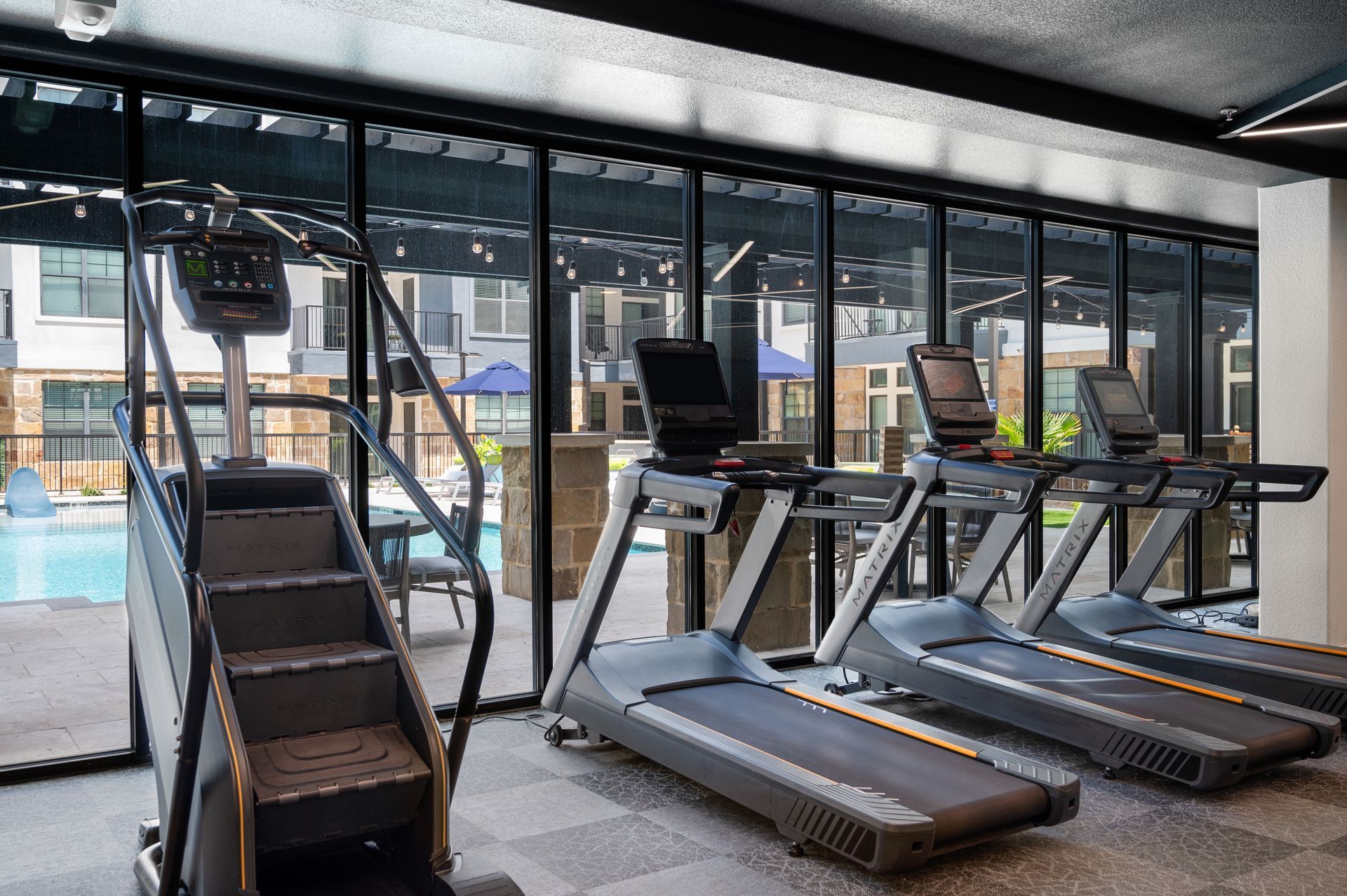 Gym with stair stepper, treadmills, and a pool view outside the windows.