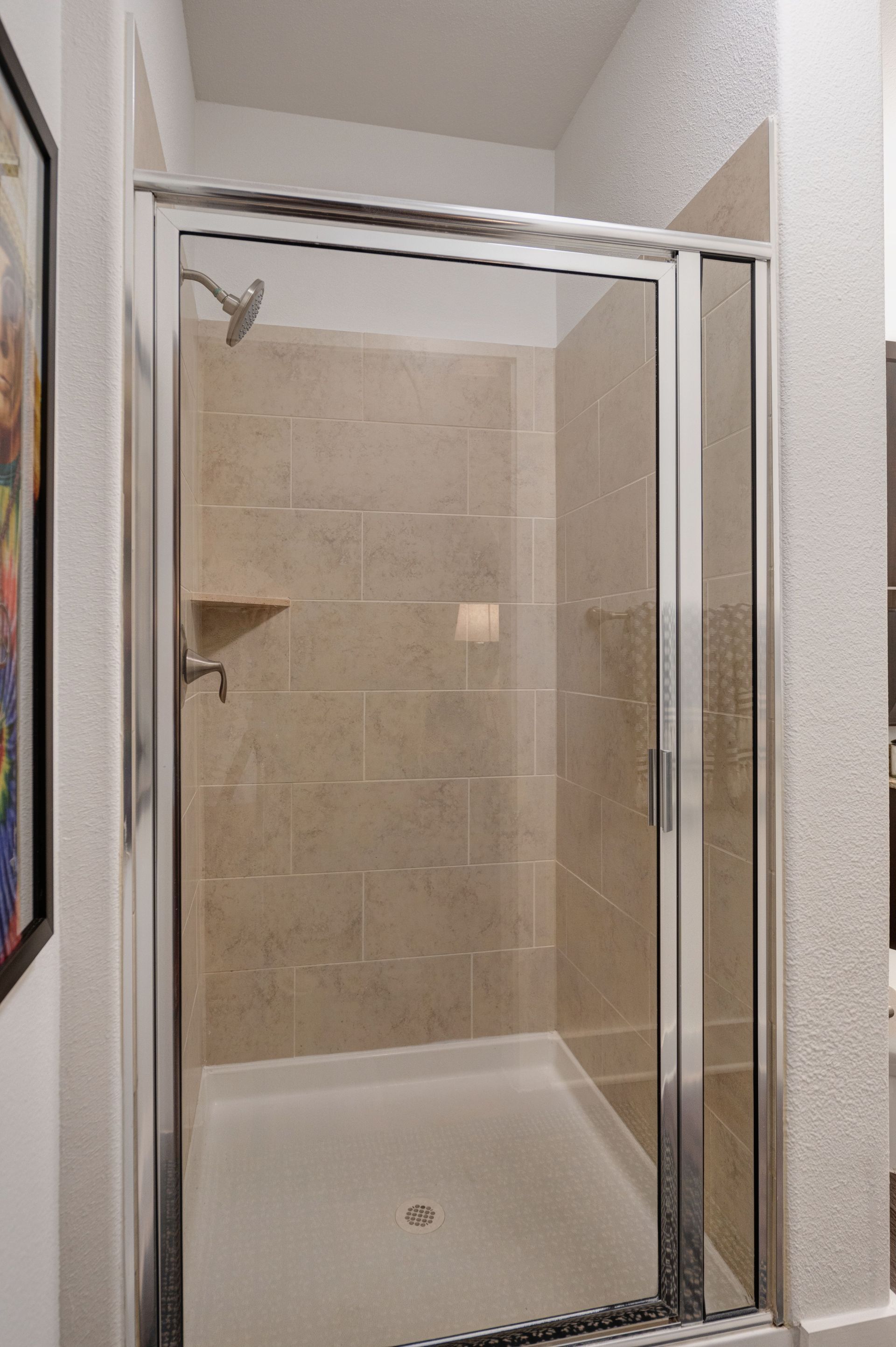 Shower stall with a glass door and tiled walls.