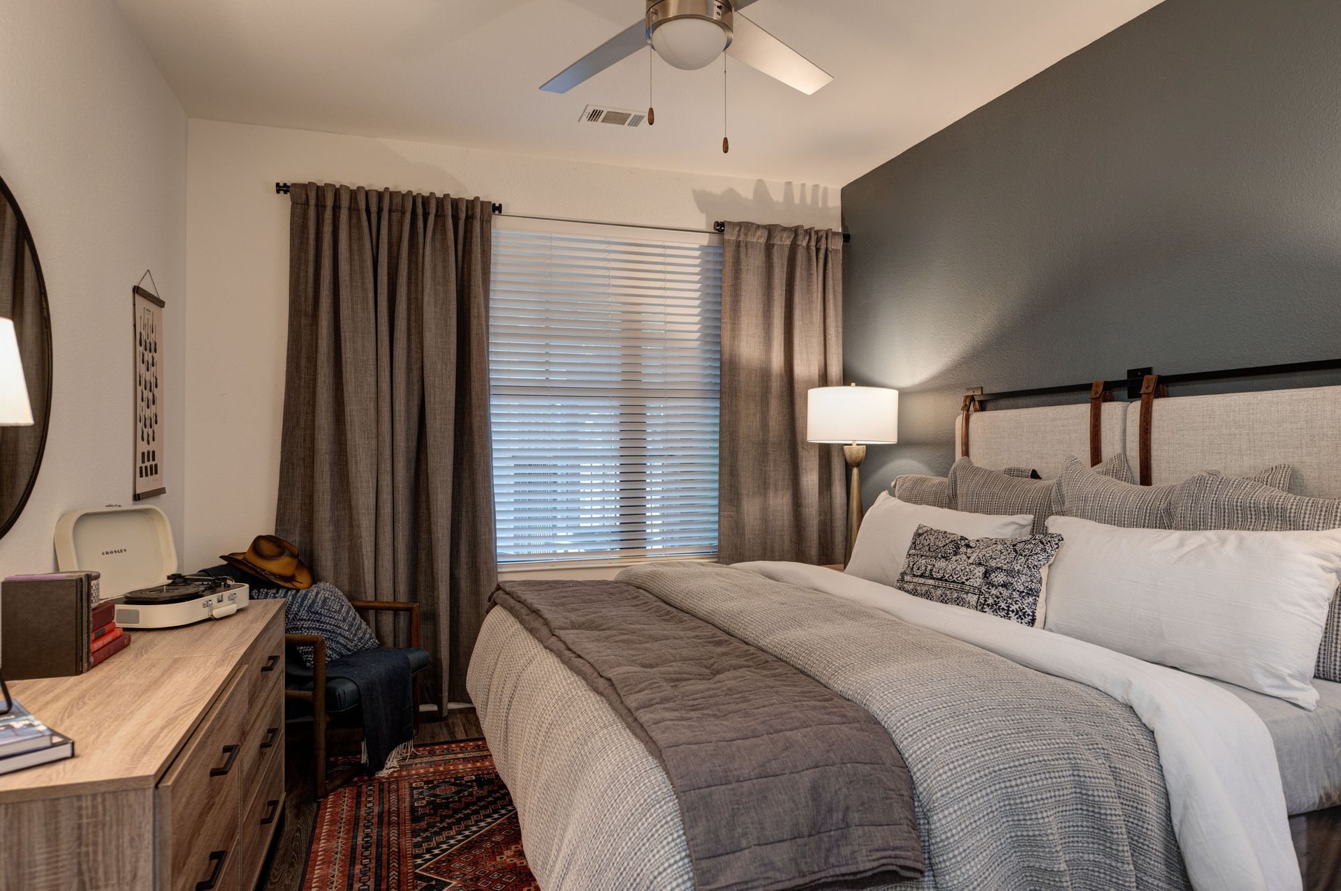 Bedroom with bed, dresser, window with blinds, and dark gray accent wall.
