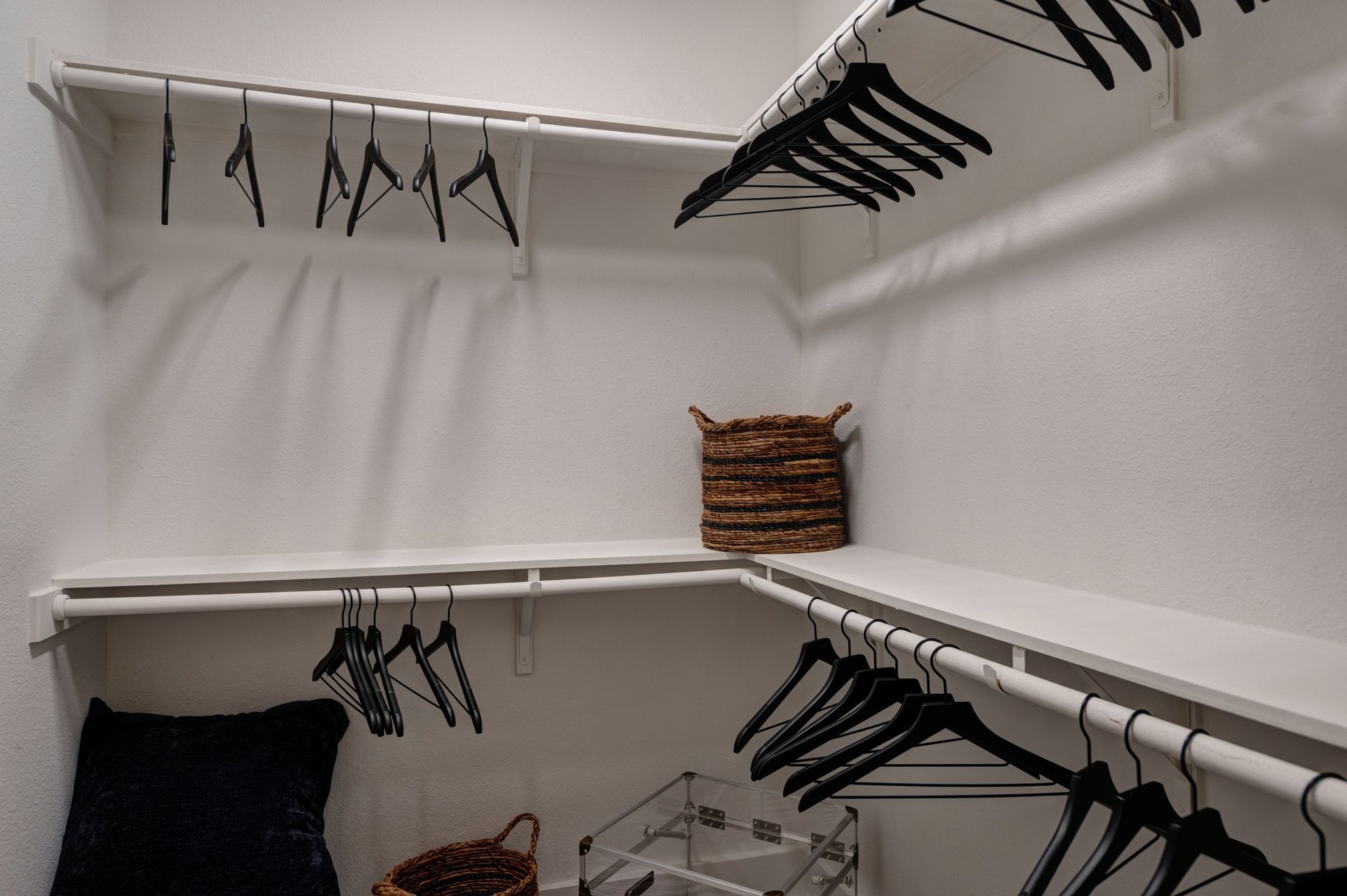 White closet with shelving, clothes hangers, and a basket.