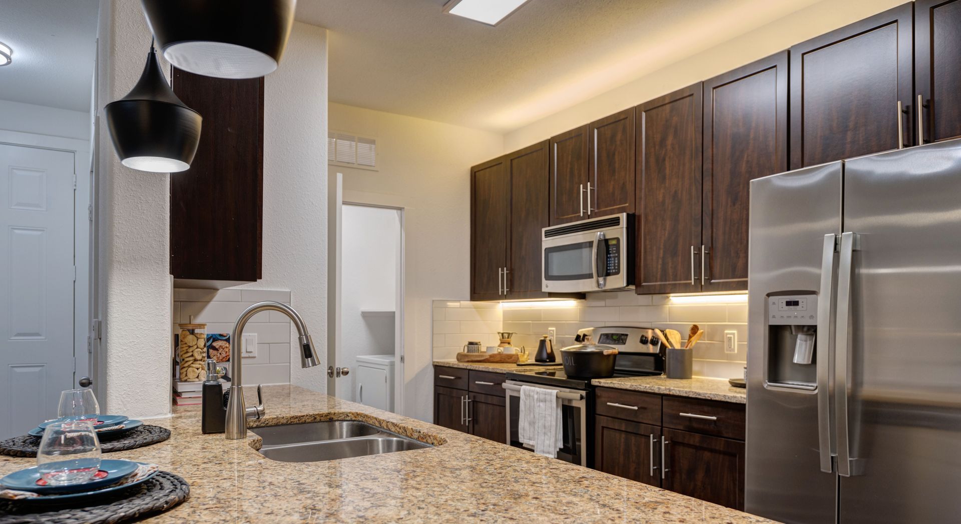 Modern kitchen with dark wood cabinets, granite countertop, stainless steel appliances, and pendant lights.