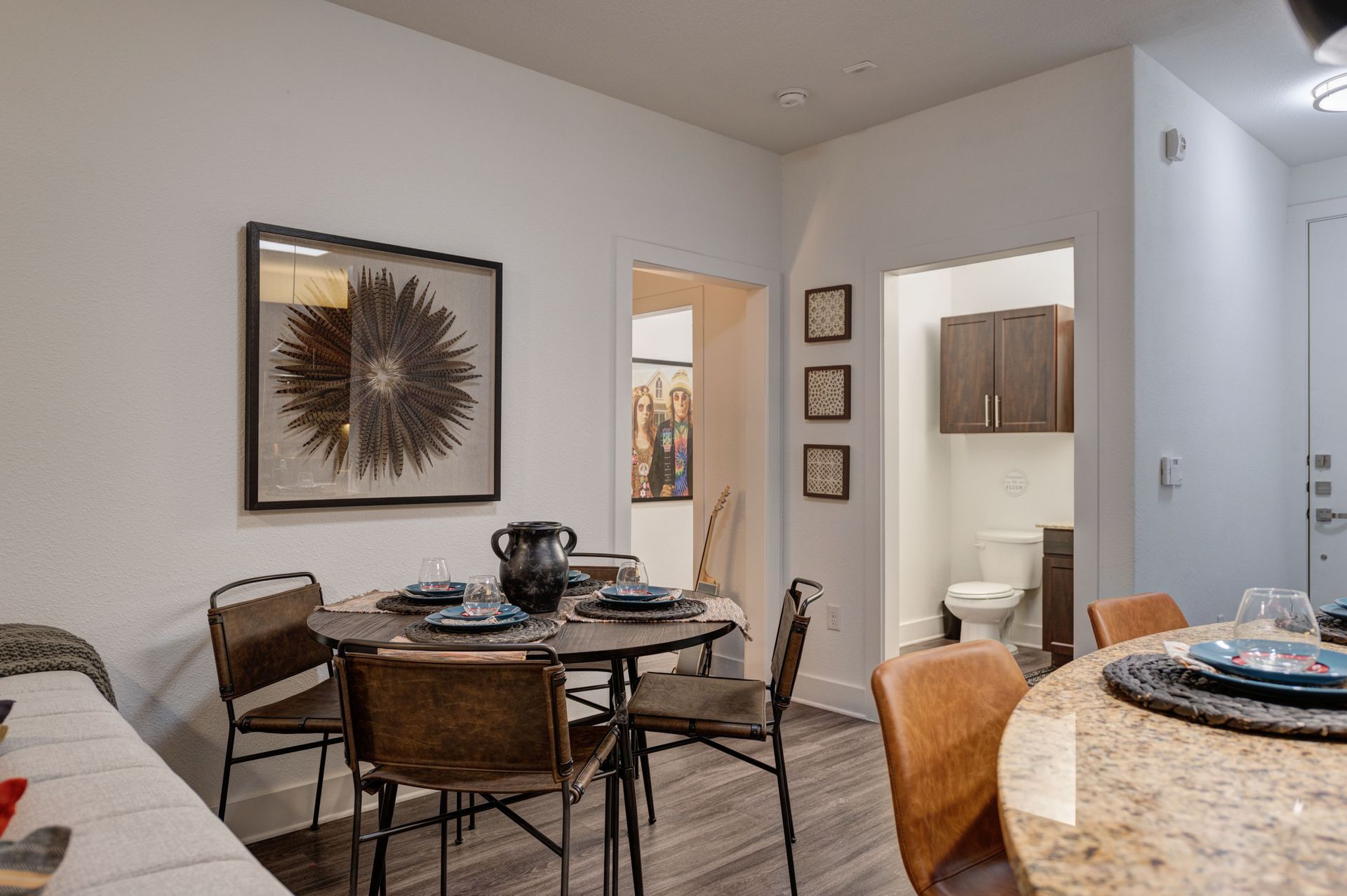 Dining area with round table, chairs, artwork, and doorway to bathroom.