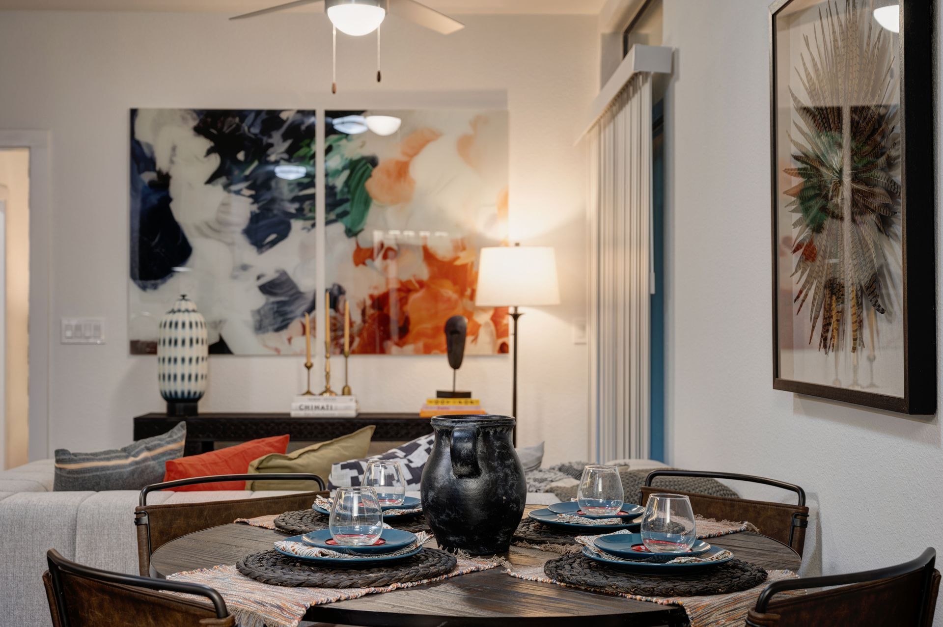 Dining room with round table set for dinner, colorful artwork on wall, sofa in background.