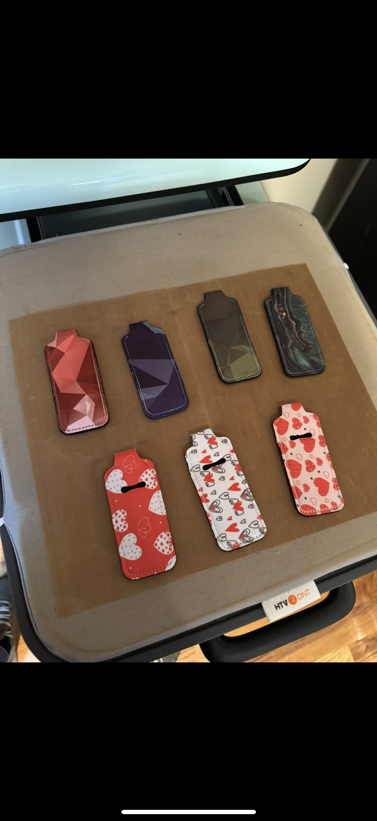 Eight patterned phone cases on a heat press with a brown pad.
