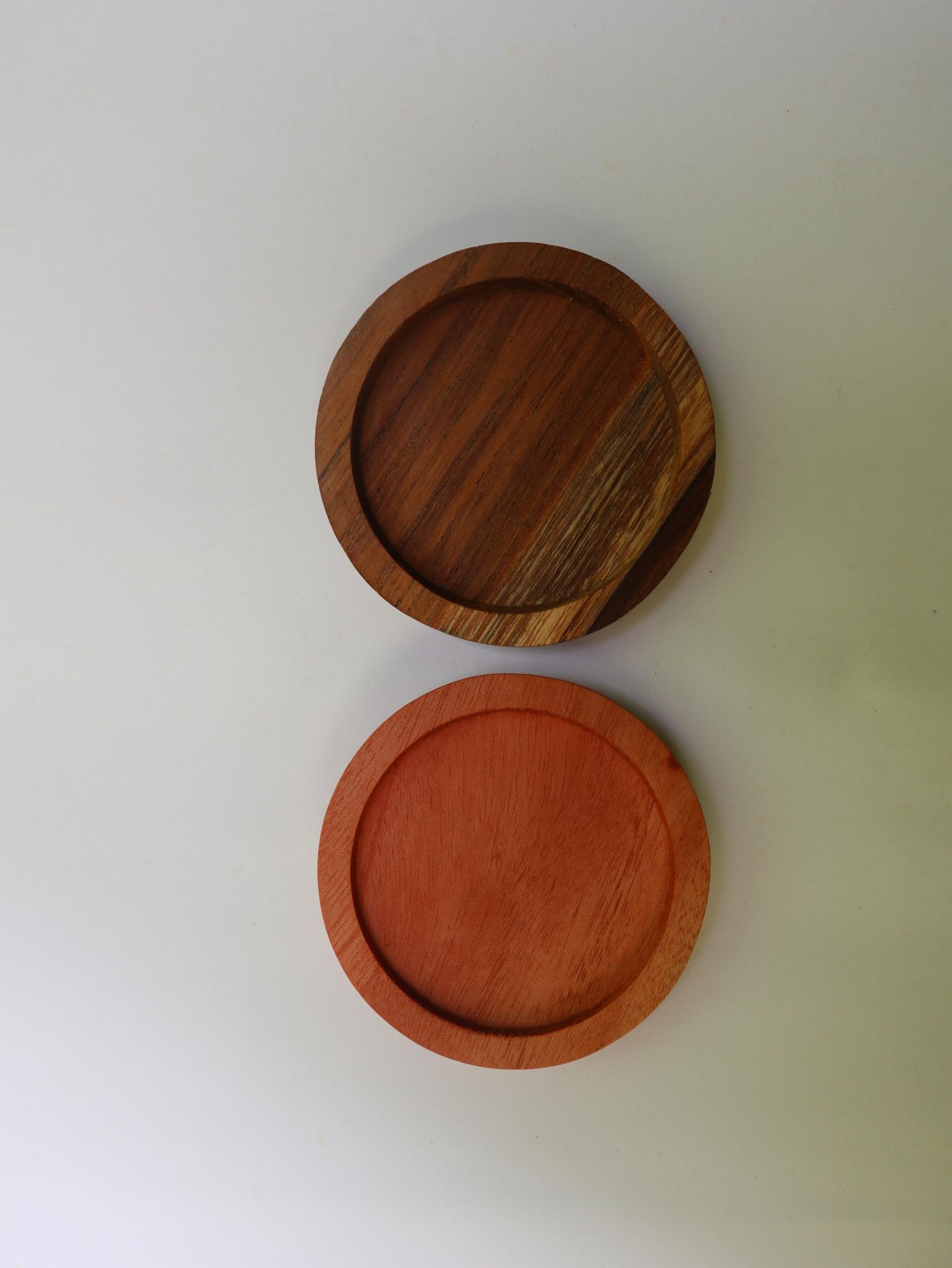 Two circular wooden coasters, one dark brown, one reddish-orange, on a white surface.
