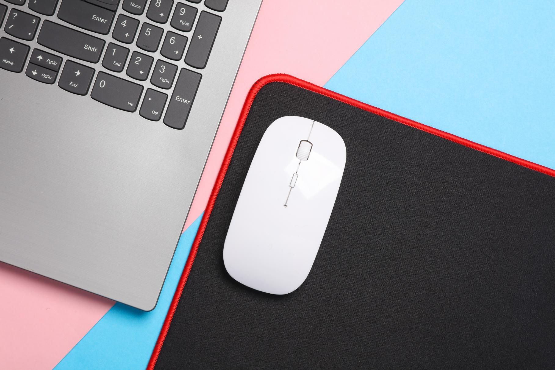 Laptop and white mouse on a black mousepad with a red border, on a pink and blue background.