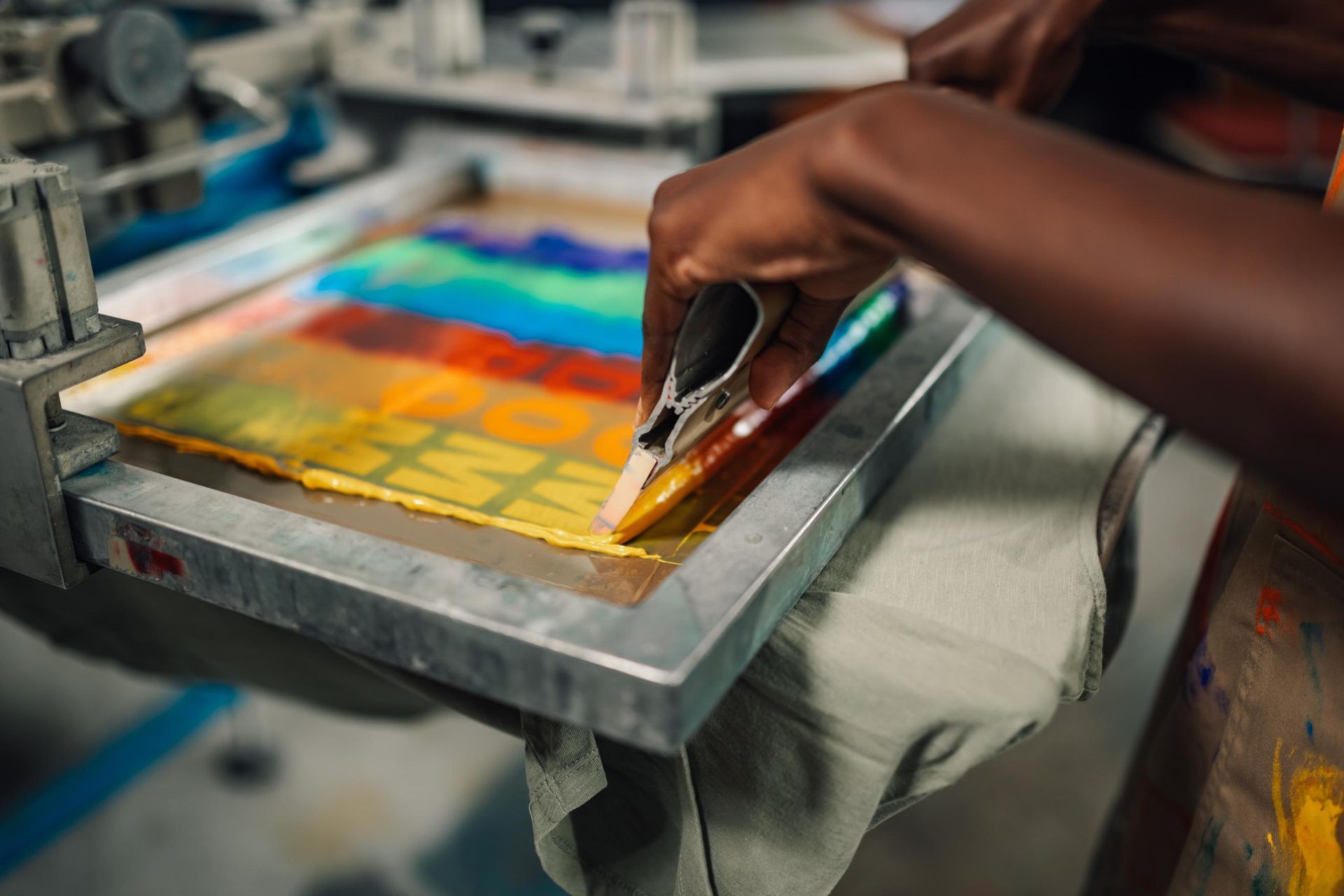 Person using a squeegee to apply rainbow-colored ink through a screen onto fabric.
