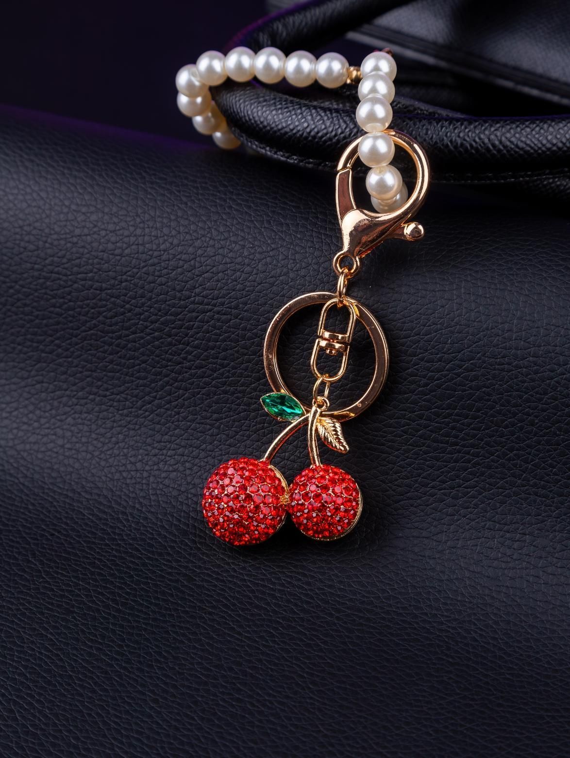 Cherry-shaped keychain with red rhinestones and a pearl-beaded handle attached to a black purse.