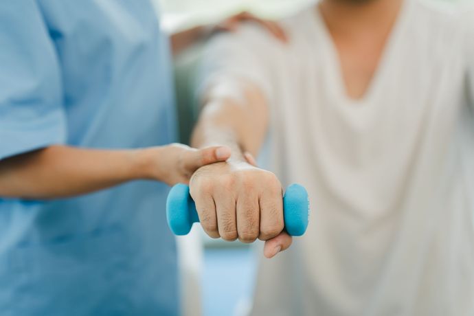 Terapista che aiuta un paziente a eseguire un esercizio con manubri blu.