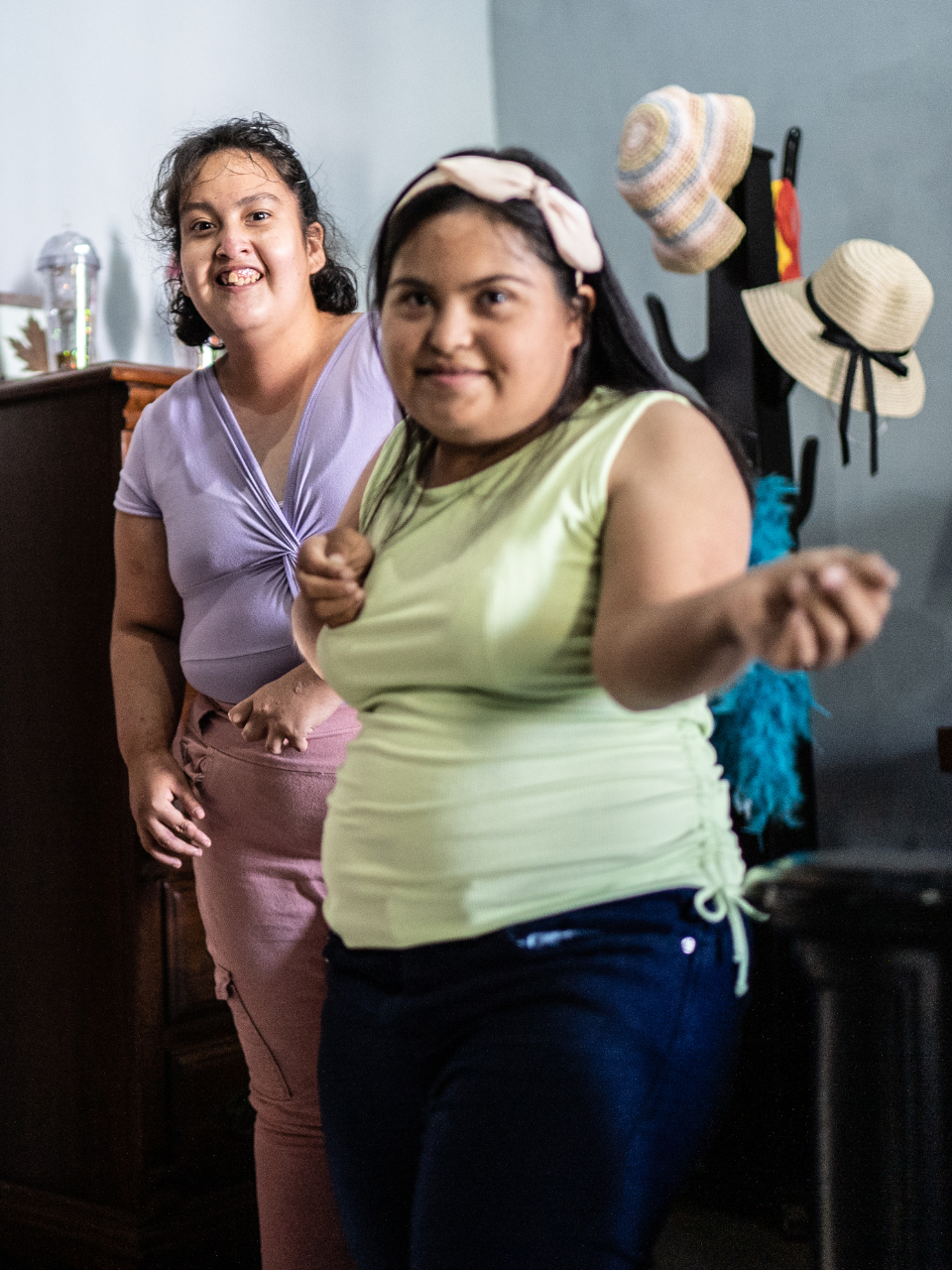 Man in a wheelchair using a laptop at a wooden table in a kitchen. He is smiling and wearing a blue shirt.