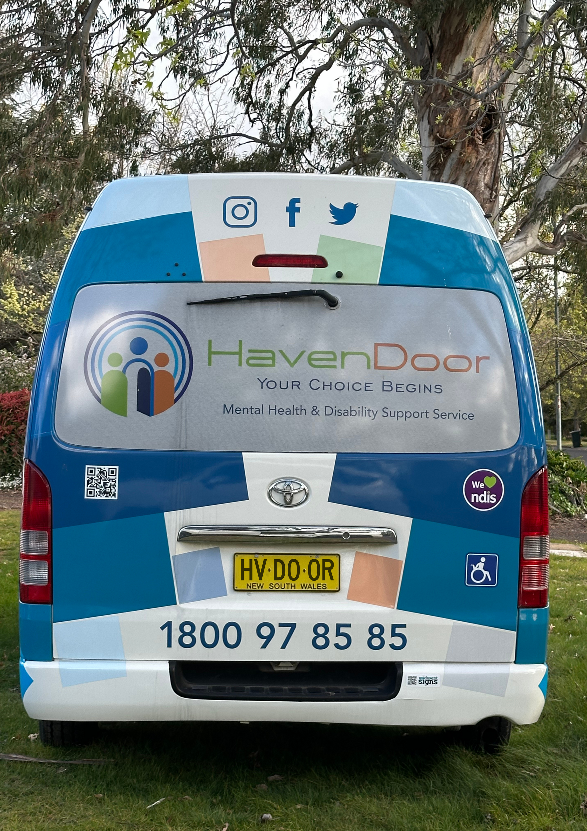 Man in wheelchair using a lift to enter a van. He wears a gray shirt, tan pants, and smiles.