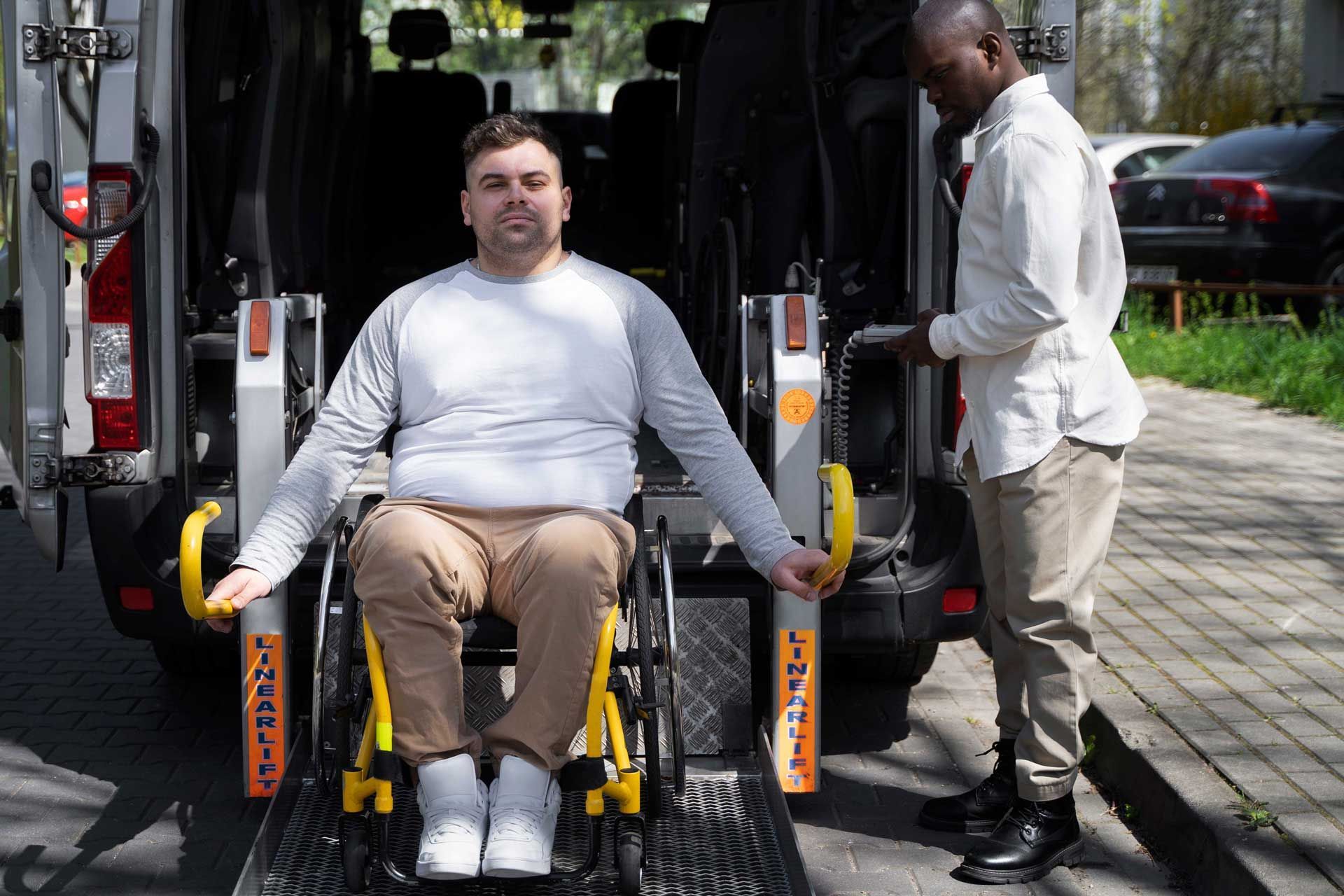 Man in wheelchair using a lift to enter a van. He wears a gray shirt, tan pants, and smiles.