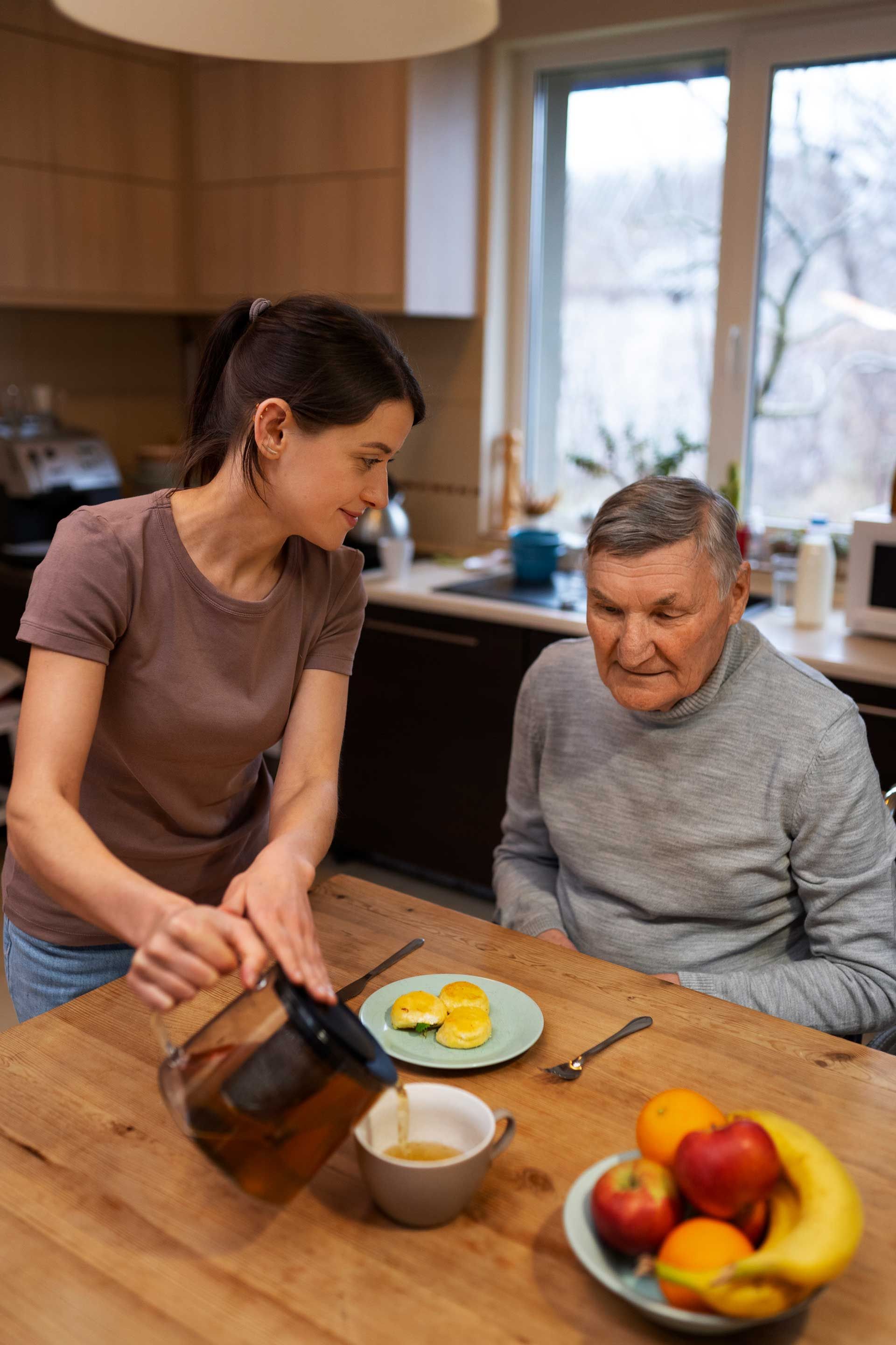 Woman pouring drink for older man at table; breakfast setting.