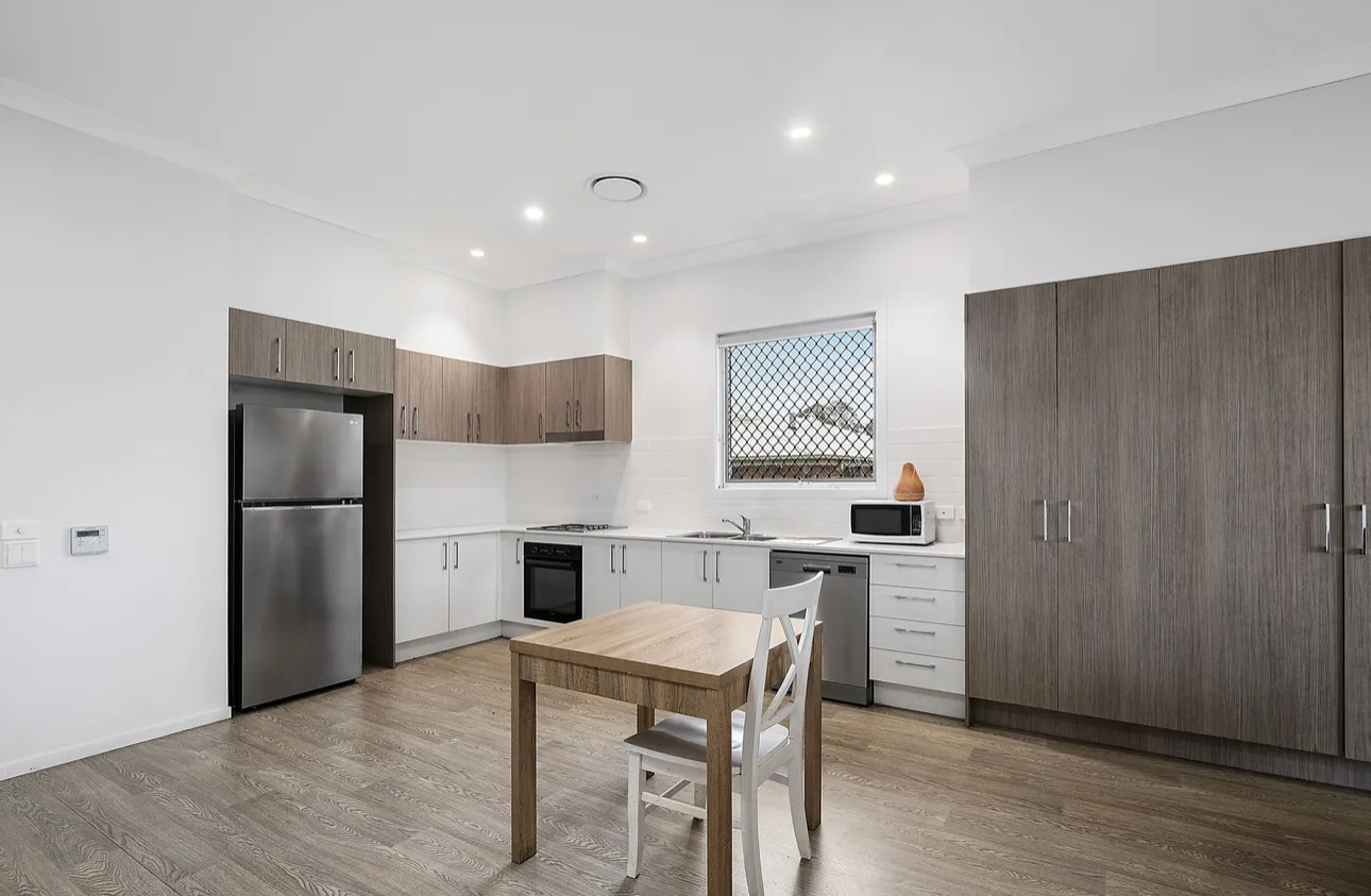 Outdoor patio with a sofa, armchairs, and a circular coffee table on a rug; lush green lawn in the background.