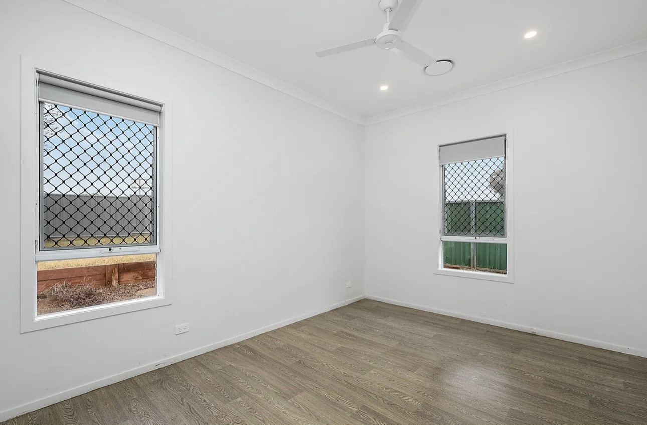 Empty bedroom with tan carpet, beige walls, white built-in closet, and window with curtains.