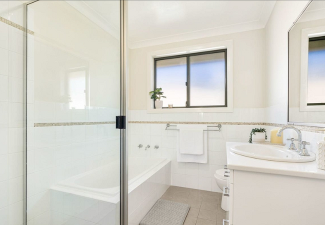 White bathroom with a bathtub, shower, sink, window, and toilet.